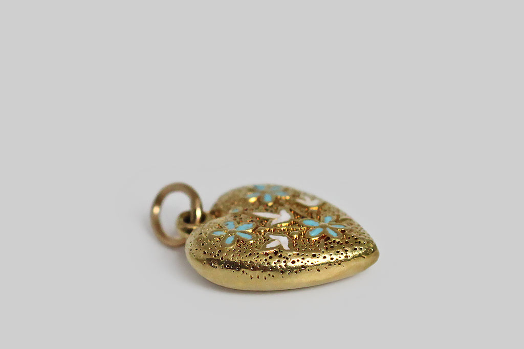 A darling, Art Deco era, heart-shaped harm, modeled in 14k yellow gold, and decorated with flowers in blue and white enamel. These little blossoms (lilies of the valley and forget me nots) sit atop the charm's finely-speckled, hand-textured surface. 