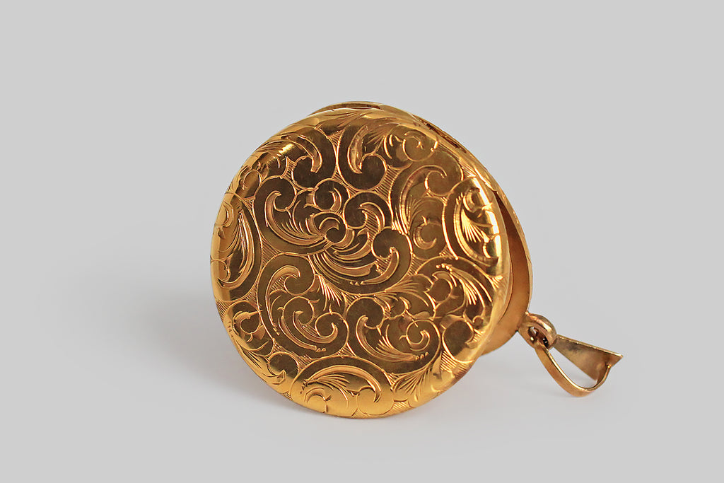 An extra-large, Victorian era locket, modeled in high-color 14k yellow gold, whose face is set with a sparkling 1/3 carat white diamond. The locket is decorated, edge-to-edge, front and back, with ornate, hand-engraved plumes and curls. A plump, languid flower rests amid these swirling forms, at the center of the locket’s face, where the diamond marks its center. This is an especially lovely old locket— the hand engraving is deep, confident, and expressive. 