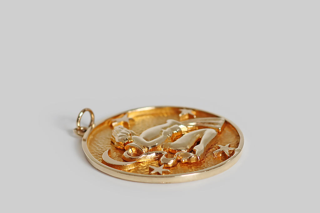 Poor Mouchette | Curated Antique Jewelry, Vintage Jewelry & Engagement Rings | Portland, Oregon | A very cool, extra-large, mid 20th century pendant, modeled in 14k yellow gold, whose subject is the water bearer, an image that represents the astrological sign Aquarius (January 20 - February 18). Our female water bearer has wavy, shoulder-length hair. Here, she kneels, in profile, surrounded by four stars and a crescent moon, pouring water from a vessel.