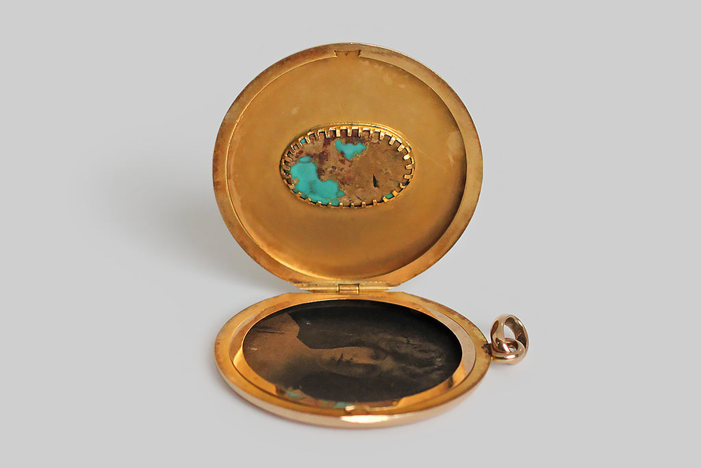 An extra-large, round, Victorian era locket, modeled in 14k rosy yellow gold, whose face is set with a single, large, matrix-webbed turquoise cabochon. This soulful, oval, blue-green gem is highly saturated, and its matrix is reddish-to-golden brown. This locket is clean, minimal, and almost contemporary felling— the earthy turquoise gem seems to float in the simple, gold pool of the locket face. The locket's reverse is hand-engraved with a large monogram, in period script