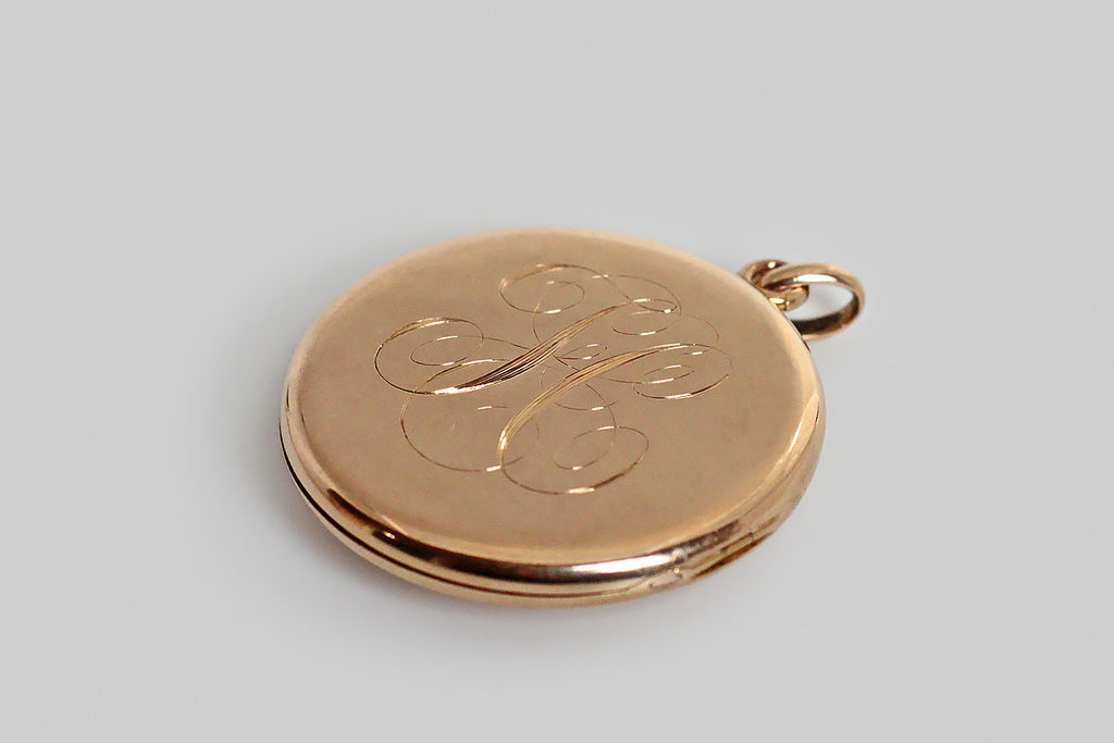 An extra-large, round, Victorian era locket, modeled in 14k rosy yellow gold, whose face is set with a single, large, matrix-webbed turquoise cabochon. This soulful, oval, blue-green gem is highly saturated, and its matrix is reddish-to-golden brown. This locket is clean, minimal, and almost contemporary felling— the earthy turquoise gem seems to float in the simple, gold pool of the locket face. The locket's reverse is hand-engraved with a large monogram, in period script