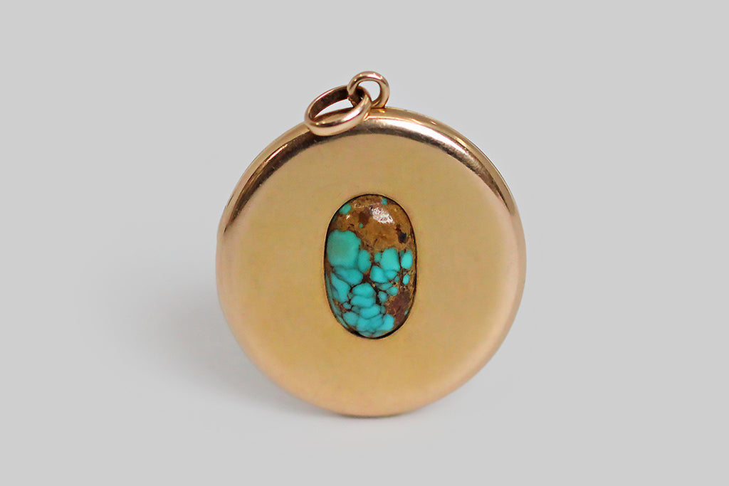 An extra-large, round, Victorian era locket, modeled in 14k rosy yellow gold, whose face is set with a single, large, matrix-webbed turquoise cabochon. This soulful, oval, blue-green gem is highly saturated, and its matrix is reddish-to-golden brown. This locket is clean, minimal, and almost contemporary felling— the earthy turquoise gem seems to float in the simple, gold pool of the locket face. The locket's reverse is hand-engraved with a large monogram, in period script