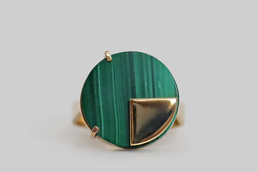 Poor Mouchette | Curated Antique Jewelry, Vintage Jewelry & Engagement Rings | Portland, Oregon | A clever, mid-20th-century, modernist ring, modeled in 18k yellow gold, whose face is set with a thick, circular malachite slab. This vivid green gem is beautifully figured with vertical stripes. It is held in a pair of angular prongs, and a high-polished, pie-slice-shaped gold sheet lays atop it, as if to signify one quarter of the whole.