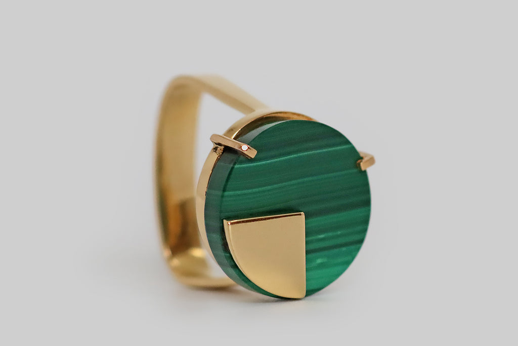 Poor Mouchette | Curated Antique Jewelry, Vintage Jewelry & Engagement Rings | Portland, Oregon | A clever, mid-20th-century, modernist ring, modeled in 18k yellow gold, whose face is set with a thick, circular malachite slab. This vivid green gem is beautifully figured with vertical stripes. It is held in a pair of angular prongs, and a high-polished, pie-slice-shaped gold sheet lays atop it, as if to signify one quarter of the whole. 