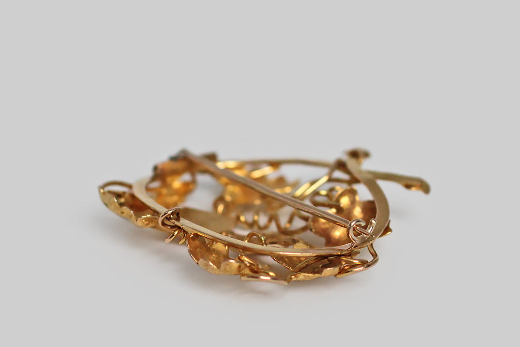 A large, Georgian-era brooch, modeled in 14k yellow gold, whose subject (a dove in flight, bearing a letter) is depicted among grapevines, grape leaves, and tendrils. Our feathered friend's message is a sentimental one— "forget me not." This brooch is primarily repoussé, which means its many, highly-dimensional elements were formed by hammering a gold sheet into relief from the reverse side. 