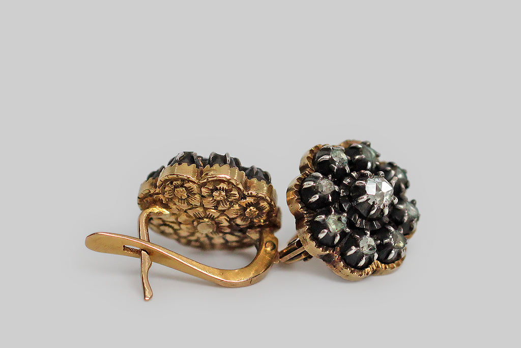 A rare and wonderful pair of dainty, Georgian, button earrings, fabricated in 14k yellow gold and silver, whose rose cut diamonds are arranged to suggest a flower. These glinty old diamonds are mounted in crimped, darkened silver collets, and those collets rest inside gold, flower-shaped, sawtooth-edge bases. The subtly-convex backsides of these earrings are decorated with the most beautiful, deeply-hand-engraved details