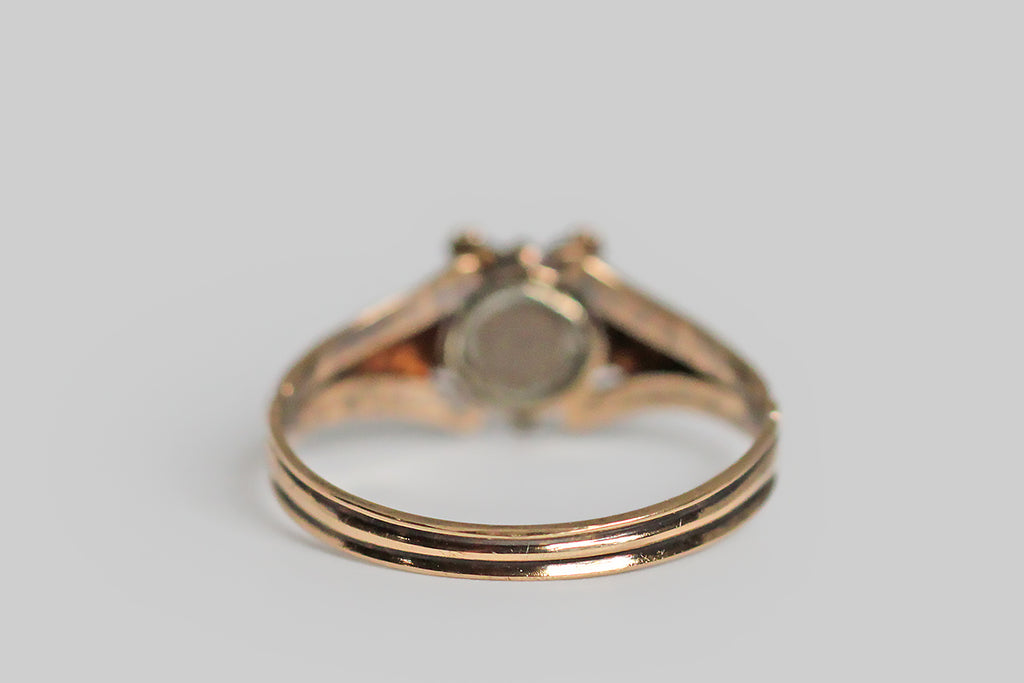 A Georgian-era pansy form ring, modeled in high karat gold, whose petals are set with faceted garnet and chrysoberyl gems. This little flower is highly-dimensional, thanks to the slight pitch of its petals, and the alternating colors of these petals add a loves me, loves me not suggestion to this traditional sweetheart motif. The ring's ornate split shoulders and reeded shank are shapely, unusual, and joined by a delicate shell-like medallion. Pansy is the "think of me" flower, 