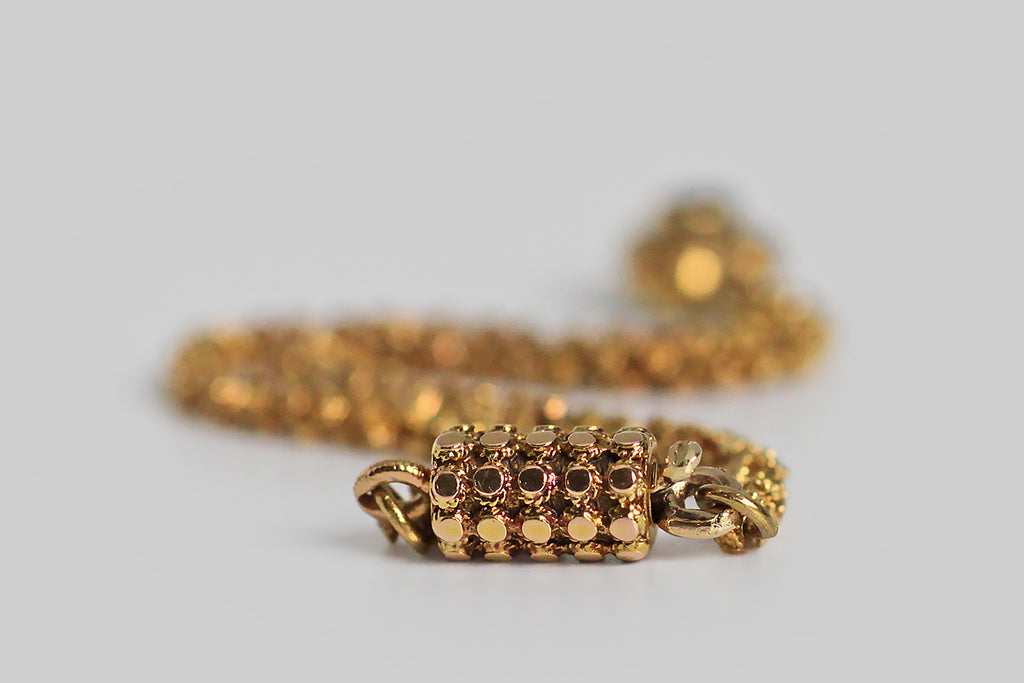 A rare and wonderful Georgian-era bracelet, whose dainty 22k gold links are each decorated with a pair of six-petaled flowers. These high-color, flower-form links encircle the wrist giving the impression of a golden garland. Our garland bracelet also features a miniature heart-shaped locket— the front side of this tiny heart is ornately hand-engraved with baroque plumes, and set with a deep-red garnet.