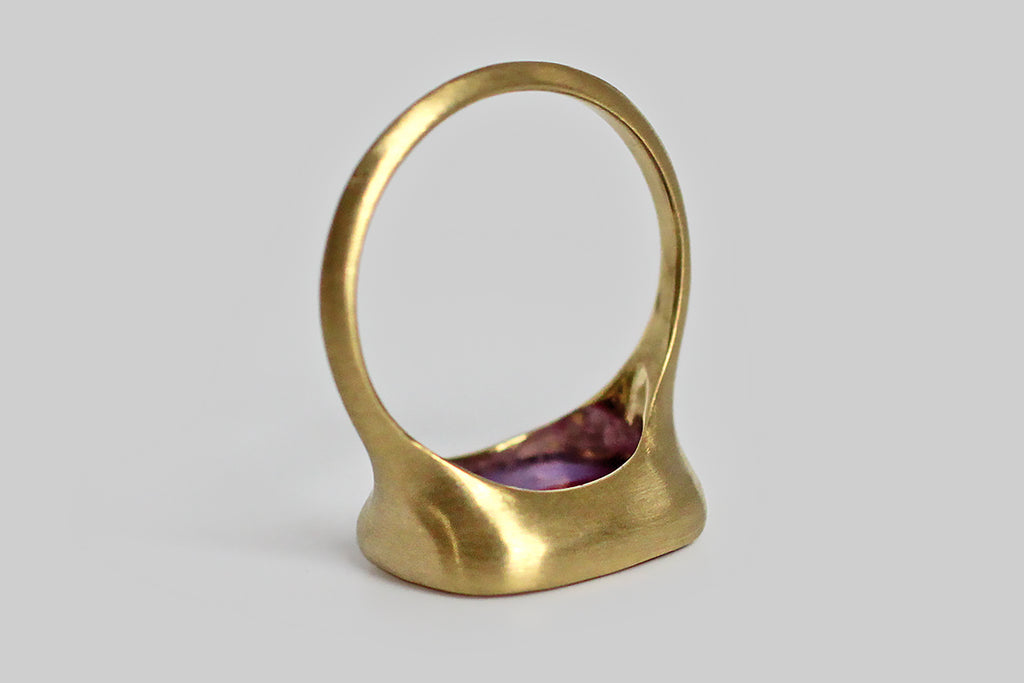 Playful and quirky, a vibrant, bi-color (violet and lavender) glass seal sits, nested, inside a thick-walled, organic bezel, which tapers seamlessly into the ring's integral shank. This unusual Victorian-era wax seal is carved with the phrase "guess & guess again"— that coy phrase would have struck the seal's owner pretty funny in the 1800s; taken out of context it is an absurd and challenging mantra