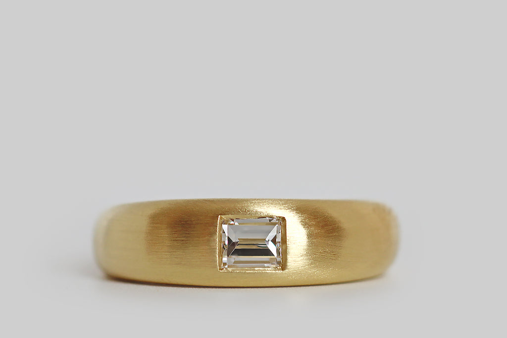 Poor Mouchette | Curated Antique Jewelry, Vintage Jewelry & Engagement Rings | Portland, Oregon | A weighty, minimalist ring, modeled in 18k yellow gold with a lightly-domed, tapering profile, whose gem is a natural, flush-set, .50 carat baguette cut diamond (E/F, VS1). This diamond is "nested" in the ring face— its crisp angles, and clean, stepped facets are a striking contrast to the band's soft, curved form. 