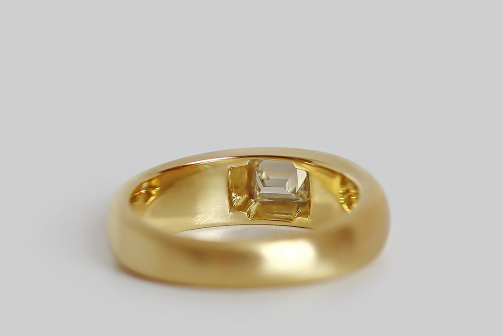 Poor Mouchette | Curated Antique Jewelry, Vintage Jewelry & Engagement Rings | Portland, Oregon | A weighty, minimalist ring, modeled in 18k yellow gold with a lightly-domed, tapering profile, whose gem is a natural, flush-set, .50 carat baguette cut diamond (E/F, VS1). This diamond is "nested" in the ring face— its crisp angles, and clean, stepped facets are a striking contrast to the band's soft, curved form.