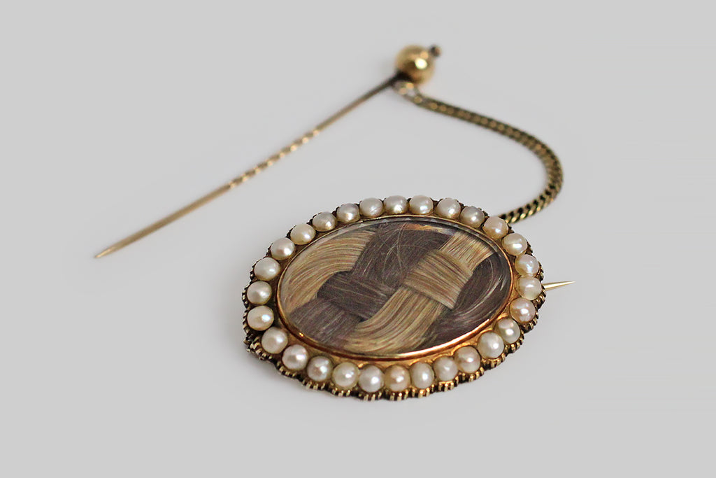 A sizable 19th century brooch, featuring two different locks of human hair (strawberry blond and silvering brunette), woven together and set beneath a beveled crystal. This plaited arrangement is encircled by an especially pretty natural pearl surround. The base of the brooch, and the many cut down collet settings are 15k yellow gold. This brooch was perhaps intended as a romantic gift for a sweetheart— its reverse is inscribed (in curling period script) "L.H. Bliss from J.B."