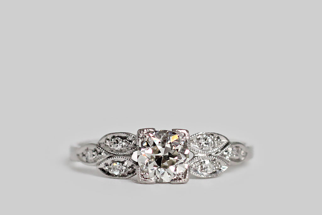Poor Mouchette | Curated Antique Jewelry, Vintage Jewelry & Engagement Rings | Portland, Oregon | An elegant, mid 20th century engagement ring, modeled in platinum, whose primary gem is a .53 carat old European cut diamond (I/J, SI1). This sparkling, hand-cut sweetheart is mounted in a low-profile, four-tab basket setting— its "picture corner" style tabs are embellished with fine milgrain. This basket is hand-pierced with a simple chevron pattern, and is flanked 