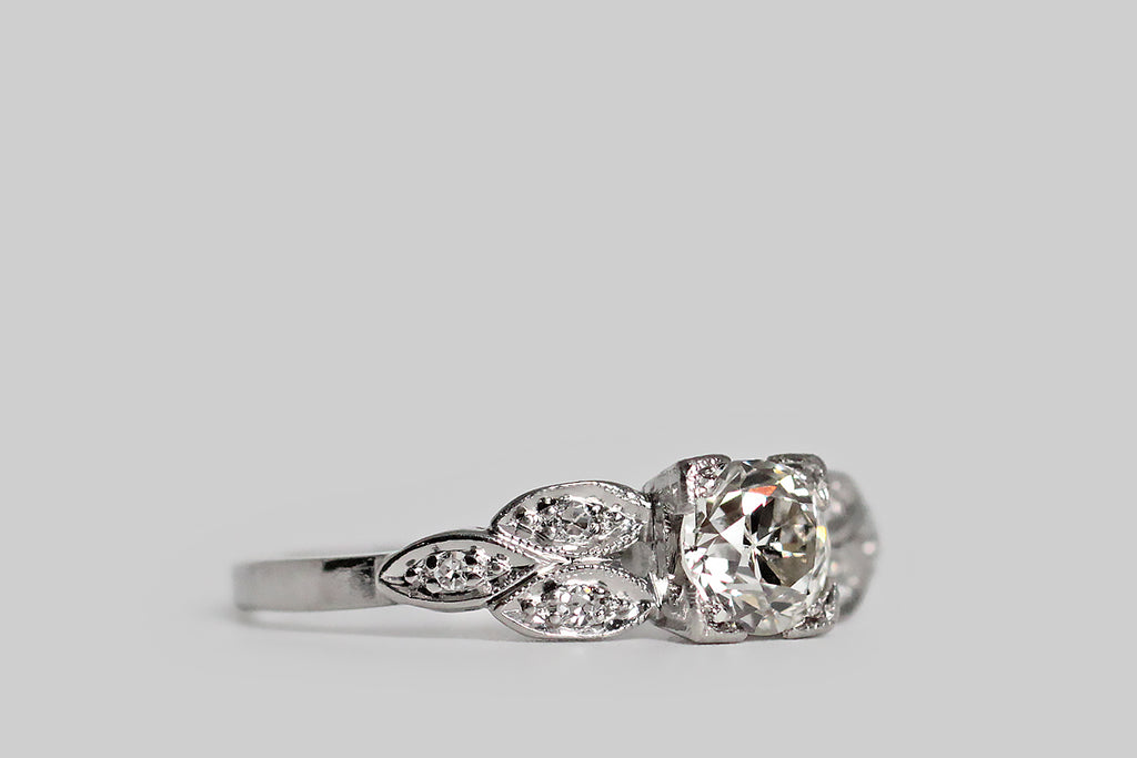 Poor Mouchette | Curated Antique Jewelry, Vintage Jewelry & Engagement Rings | Portland, Oregon | An elegant, mid 20th century engagement ring, modeled in platinum, whose primary gem is a .53 carat old European cut diamond (I/J, SI1). This sparkling, hand-cut sweetheart is mounted in a low-profile, four-tab basket setting— its "picture corner" style tabs are embellished with fine milgrain. This basket is hand-pierced with a simple chevron pattern, and is flanked