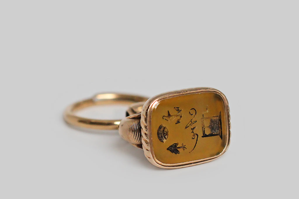 A wonderful, early-Victorian wax seal fob, modeled in 15k rose gold, whose bezel-set, agate (carnelian) seal features an intaglio carved rebus. This rebus puzzles out to mean: I hope you are well! An anchor was the popular symbol for hope during the Victorian era, and the tree in this diagram is a Yew tree. The fob itself is classically formed, with a broad stirrup-shaped arch, a round finial bail, and fine, hand-engraved lines, both straight and pinwheeling.