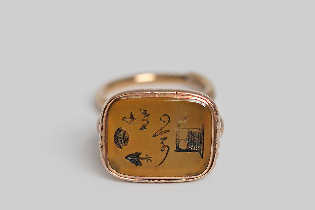 A wonderful, early-Victorian wax seal fob, modeled in 15k rose gold, whose bezel-set, agate (carnelian) seal features an intaglio carved rebus. This rebus puzzles out to mean: I hope you are well! An anchor was the popular symbol for hope during the Victorian era, and the tree in this diagram is a Yew tree. The fob itself is classically formed, with a broad stirrup-shaped arch, a round finial bail, and fine, hand-engraved lines, both straight and pinwheeling.