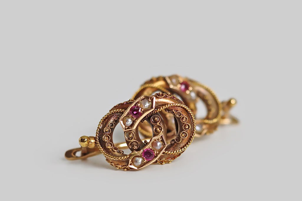 Poor Mouchette | Curated Antique Jewelry, Vintage Jewelry & Engagement Rings | Portland, Oregon | A pair of Victorian-era, Etruscan revival earrings, modeled in 14k rose gold, whose beautiful form resembles a pair of joined rings. These interlocking rings are hollow-form, thick-walled, and fully-dimensional. They are ornately decorated with intricate, twisted wire work, and beads of granulation. Trios of gemstones (ruby and seed pearl) decorate the applied, banner-like seats that rest atop the rings. 