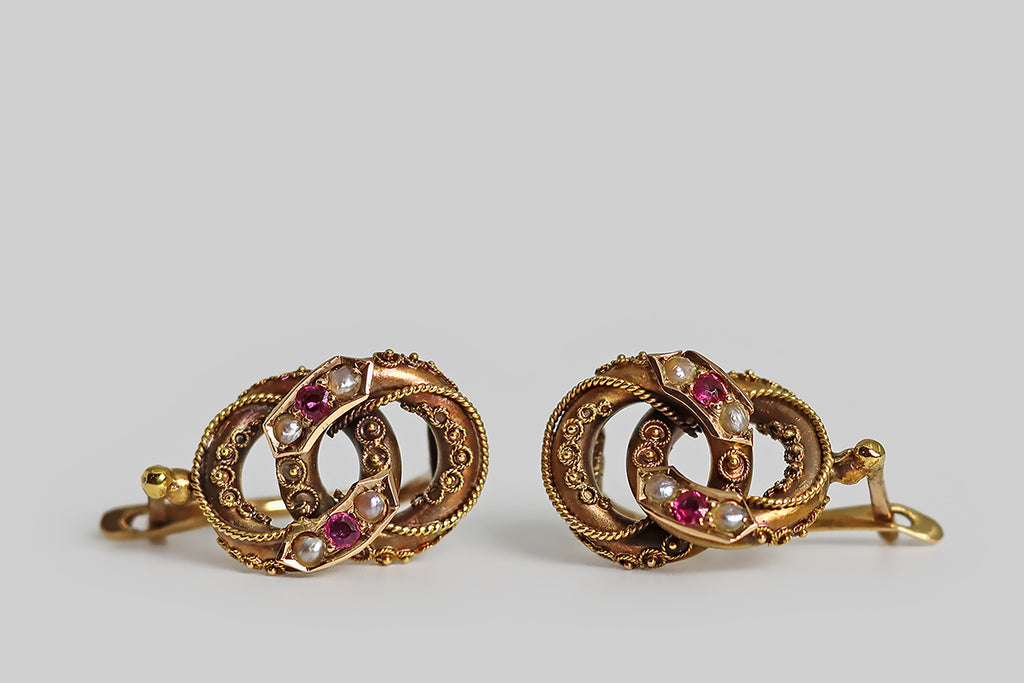 Poor Mouchette | Curated Antique Jewelry, Vintage Jewelry & Engagement Rings | Portland, Oregon | A pair of Victorian-era, Etruscan revival earrings, modeled in 14k rose gold, whose beautiful form resembles a pair of joined rings. These interlocking rings are hollow-form, thick-walled, and fully-dimensional. They are ornately decorated with intricate, twisted wire work, and beads of granulation. Trios of gemstones (ruby and seed pearl) decorate the applied, banner-like seats that rest atop the rings.