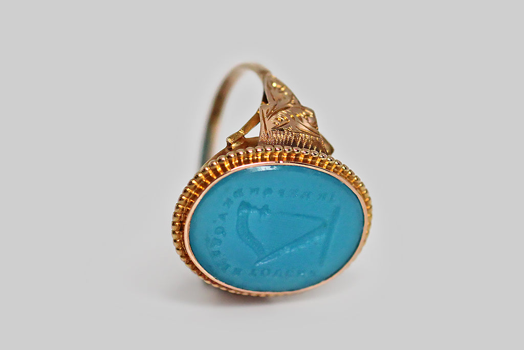 An especially rare and ephemeral Georgian era signet ring, mwhose turquoise glass intaglio seal is carved with an image of a harp, surrounded by the phrase “je reponds á qui me touche:” I respond to every touch. This beautiful old Tassie seal is still partnered with its original high karat gold ring mount. 