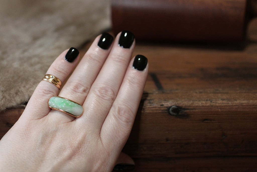 An elegant, large-scale, vintage saddle ring, modeled in 14k yellow gold, featuring a carved, moss in snow, jadeite jade cabochon. This natural, untreated, "A" jade cabochon is held held in a smooth, low-profile bezel— it has been cut on a curve to create the classic saddle shape of the ring, and is set low, so that the cool jade lays against the wearer's skin. This jade cabochon is snow white, with trailing light green figuring. It is carved with soft botanical forms