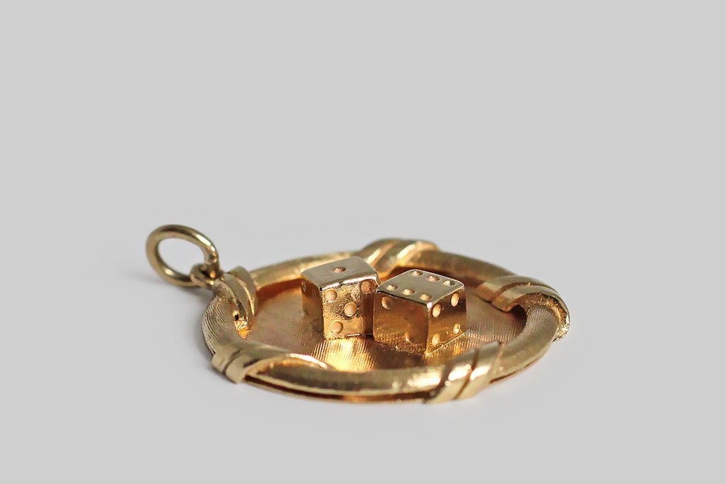 Poor Mouchette | Curated Antique Jewelry, Vintage Jewelry & Engagement Rings | Portland, Oregon | A wonderful, weighty, mid 20th century charm, modeled in 14k yellow gold, featuring a pair of three dimensional dice, displaying six pips and one pip— lucky seven ! This large, disc-shaped charm has a slightly-proud, curling, double-ribbon border. The dice rest atop the charm's finely-textured field.