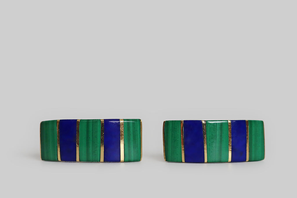 A very cool pair of late-vintage earrings, modeled in 18k gold, with strong, geometric design principles. These earrings are bar-like and slightly curved, so they read almost like a half-hoop, in wear. Vibrant, horizontally-set slabs of inlaid lapis and malachite cover their faces, where these blocks of color are divided by slender strips of yellow gold. 