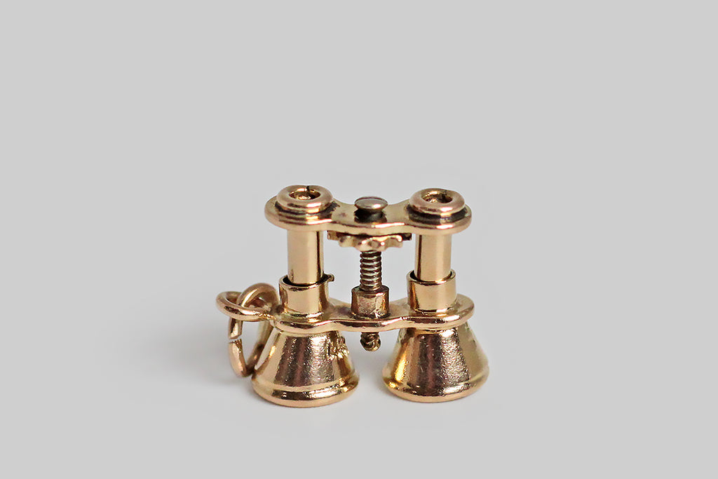 A darling, mid 20th century charm, modeled in 14k yellow gold as a highly realistic pair of binoculars. These miniature field glasses are made with many individually fabricated parts, which makes them appear mechanical— the central post is actually threaded, the ratcheting disc is complete with tiny, hand-sawed notches, and the screw head looks like you could really turn it with a screw driver! We love these finely-made old charms, and like our favorite examples, this one has lots of symbolic potential.