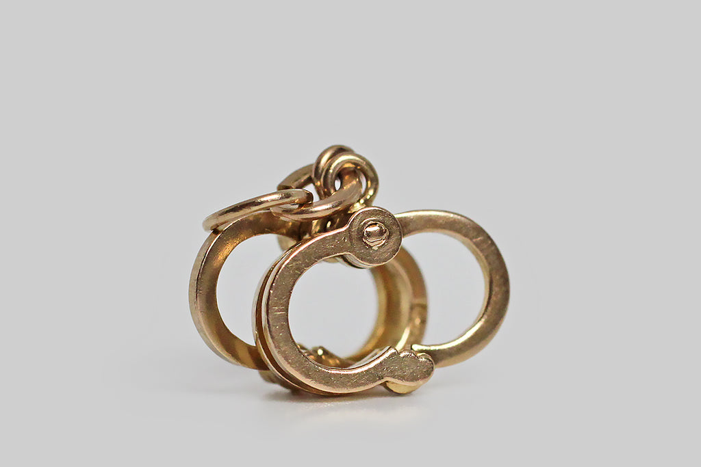 A darling, mid 20th century charm, modeled in 14k yellow gold, as a very realistic pair of handcuffs. These functioning, miniature restraints are handmade and highly detailed— to open them, gently squeeze the the two-piece side, and pull the one-piece away from it! We love these finely-made old charms, and like our favorite examples, this one has lots of symbolic potential. 