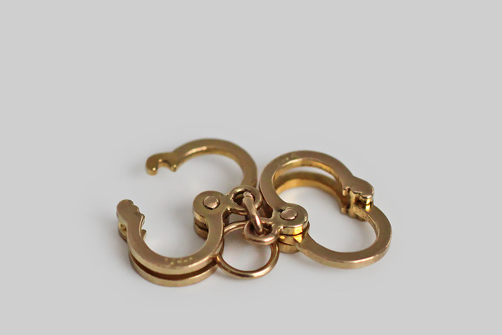 A darling, mid 20th century charm, modeled in 14k yellow gold as a very realistic pair of handcuffs. These functioning, miniature restraints are handmade and highly detailed— to open them, gently squeeze the the two-piece side, and pull the one-piece side away from it! We love these finely-made old charms, and like our favorite examples, this one has lots of symbolic potential. 