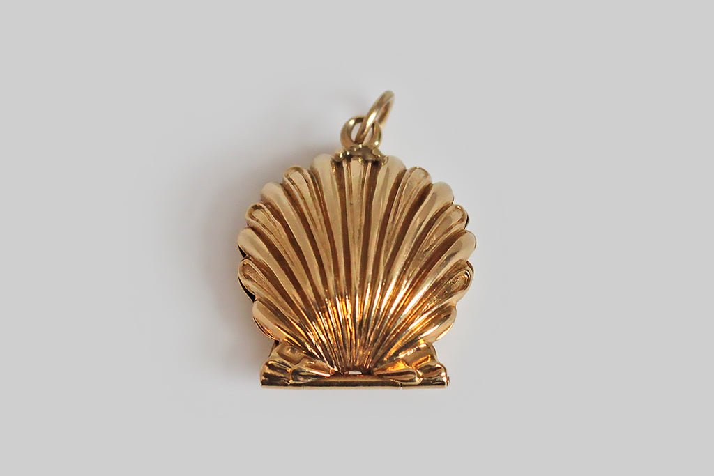 A darling, mid 20th century mechanical charm, modeled in 14k yellow gold, as a seashell that conceals a small white pearl. This little shell has a delicate scalloped form, and the alternating smooth and textured rays of the shell face make it extra pretty. This opens and closes with a latching mechanism— a small bead functions as the push-off. 