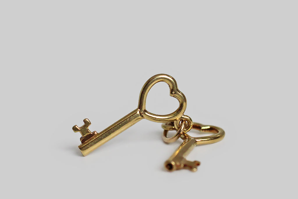 A very sweet mid 20th century charm, modeled in 14k yellow gold, whose subject is a miniature pair of keys, with heart shaped tops. These little keys hang separately on their jump ring, and jangle pleasantly with movement. There’s the classic “keys to my heart” reading available here, but because there are two keys present, and only one person holds them, we also have a little room for alternative symbolic