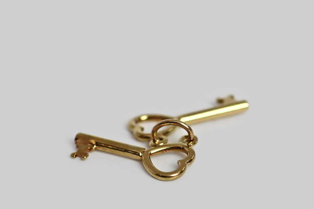 A very sweet mid 20th century charm, modeled in 14k yellow gold, whose subject is a miniature pair of keys, with heart shaped tops. These little keys hang separately on their jump ring, and jangle pleasantly with movement. There’s the classic “keys to my heart” reading available here, but because there are two keys present, and only one person holds them, we also have a little room for alternative symbolic