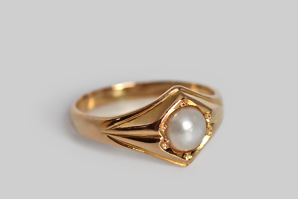 A shapely, mid-twentieth-century ring, modeled in 18k yellow gold and set with a luminous, white, button-shaped, saltwater pearl. This ring’s perfectly balanced form is two-peaked, with simple, deeply-carved shoulder details that are reminiscent of folded paper or fabric. This is simple, elegant, and mystical-seeming, bearing some resemblance to anthroposophical designs. T