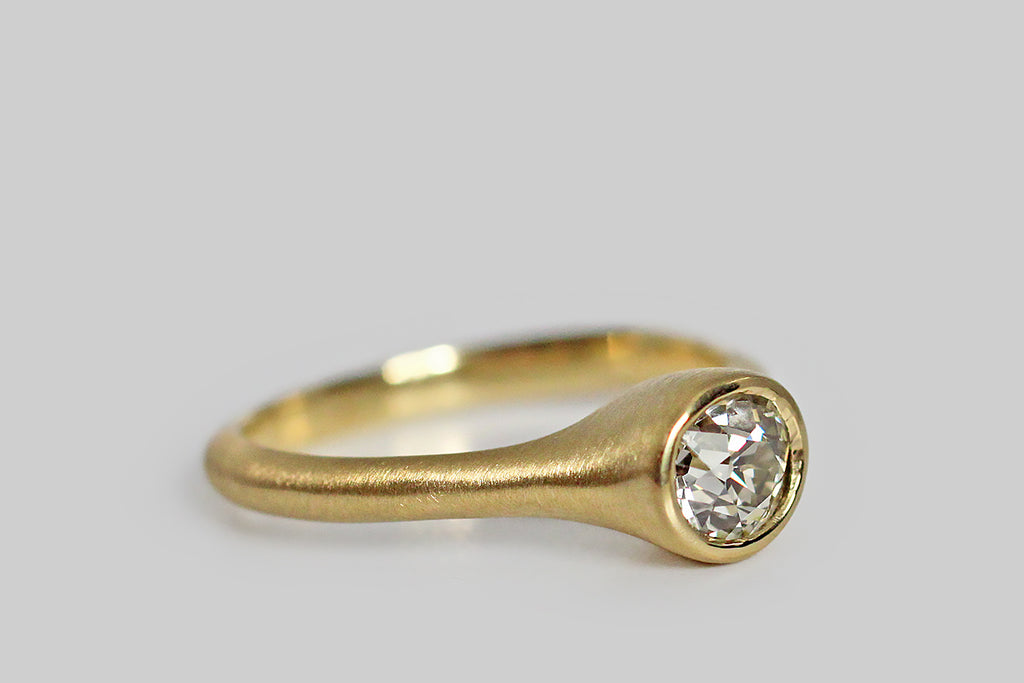 Soulful and sparkling, an antique, .70 carat old mine cut diamond sits, nested, inside a thick-walled, organic bezel, which tapers seamlessly into its ring's integral shank. This ring is modern and organic— its graceful shape is reminiscent of the beautiful pixie cup lichens (Cladonia asahinae). Metal is 18k yellow gold; it is delicately brushed. Old mine cut diamonds are much loved by collectors for their unique, hand-cut character, their small, high, tables, open culets, and off-round shape.