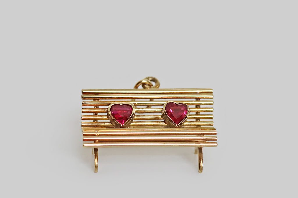 Poor Mouchette | Curated Antique Jewelry, Vintage Jewelry & Engagement Rings | Portland, Oregon | A sweet, sentimental, vintage charm, realistically hand-fabricated in 14k yellow gold, to recall a park bench. This miniature bench is made of a series of round gold wires, that perch atop hand-pierced legs— these "slats" curve to create a cozy, realistic bench seat. A pair of bezel-set, heart-shaped rubies rest on our bench, symbolizing two lovers.