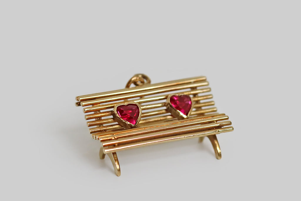 Poor Mouchette | Curated Antique Jewelry, Vintage Jewelry & Engagement Rings | Portland, Oregon | A sweet, sentimental, vintage charm, realistically hand-fabricated in 14k yellow gold, to recall a park bench. This miniature bench is made of a series of round gold wires, that perch atop hand-pierced legs— these "slats" curve to create a cozy, realistic bench seat. A pair of bezel-set, heart-shaped rubies rest on our bench, symbolizing two lovers.