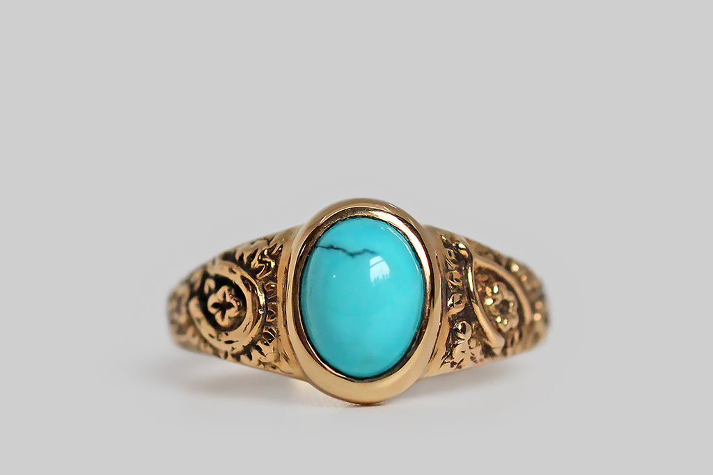 The Periapt ring, modeled 14k yellow gold, in the image of a beloved Victorian era jewel, and featuring a brilliant-blue, Sleeping Beauty turquoise cabochon. Our Periapt ring is so-called because its carved decor is a collection of lucky charms: a horseshoe, a wishbone, and a handful of four leaf clovers . . . a spattering of cheerful flowers flesh out the design. This ring is substantially made, with a classic tapering profile, and its turquoise gem is bezel set. It is ideal for frequent wear. 
