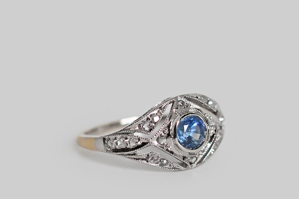 Poor Mouchette | Curated Antique Jewelry, Vintage Jewelry & Engagement Rings | Portland, Oregon | A delicate, Edwardian-era engagement ring, modeled in 18k yellow gold, with a platinum-foiled top, whose central gem is a natural, medium-blue, Ceylon sapphire (approx .40 carats). This ethereal old beauty features an intricate, diamond-studded, open-work face, replete with fine, milgrain details. The cool-blue sapphire is set in a floating bezel, and the ring's scattered, glinting, rose cut diamonds 