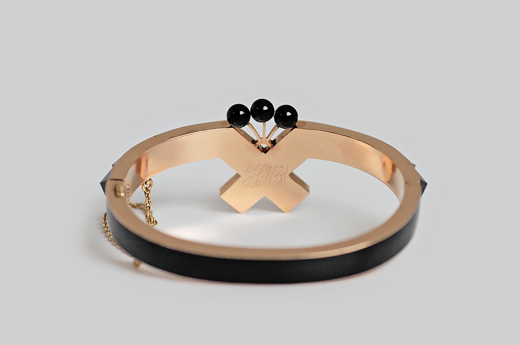 A striking Victorian-era hinged bangle, modeled in 14k rose gold to resemble a mourning ribbon, whose face is set with a series of crisp jet (RI confirmed) pyramids. This crossed ribbon is crowned with a plume-like group of three jet spheres; the backside of the bangle is inlaid with black enamel. 