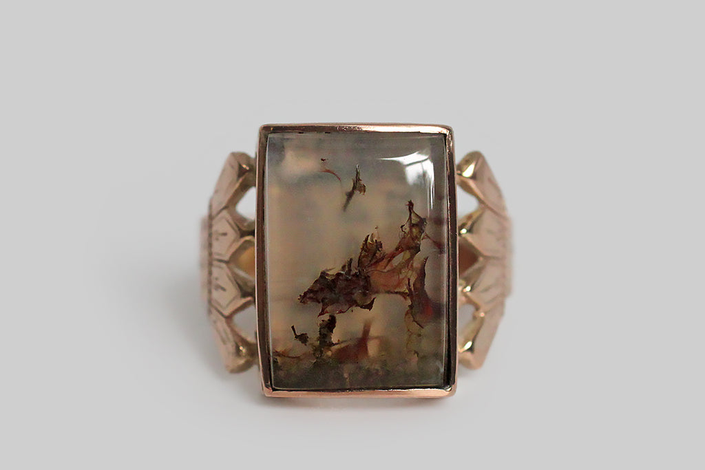 An unusual, Victorian-era, locket ring, with a sliding function, whose rectangular face is set with an outstanding plume agate cabochon. This translucent agate has highly-figural plume inclusions that read like a tender pair of tree or mushroom friends, leaning into one another on the floor of a tiny forest. The ring’s locket function is very discreet and is not noticeable when the face is closed. Its ornate, four-tine shoulders are deeply-engraved; its flat shank is weighty and broad.