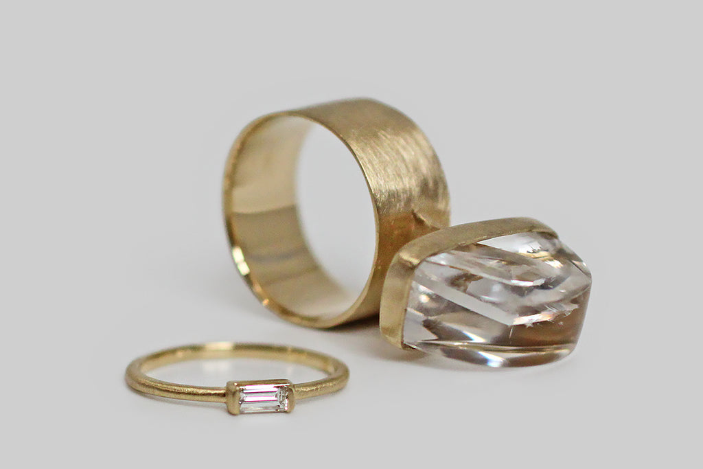 A big, mystical, modernist ring, modeled in 14k yellow gold, that features a rare, axe-head-shaped quartz-in-quartz cabochon. The "mother" quartz, here, is especially fine and optically clear— it holds within it a beautifully formed, iridescent, quartz crystal point that grew into the clear host. This inspiring specimen is mounted north to south, and is seated in a full bezel— it perches atop a shapely, flat pier that connects the ring's head to its wide, flat band. 