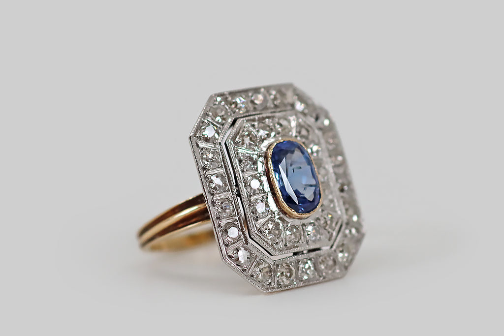 Antique Jewelry Portland, Vintage Jewelry Portland , Antique Engagement Rings | Poor Mouchette | An elegant Edwardian era panel ring, modeled in 14k rosy yellow gold, with a platinum top. The ring face features a medium blue, natural Ceylon sapphire (oval), which is haloed by a pair of delicate, octagonal, diamond-set surrounds. This double surround appears to "float," thanks to its delicate two-piece construction, and the thin negative space left between the haloes' milgrained edges.