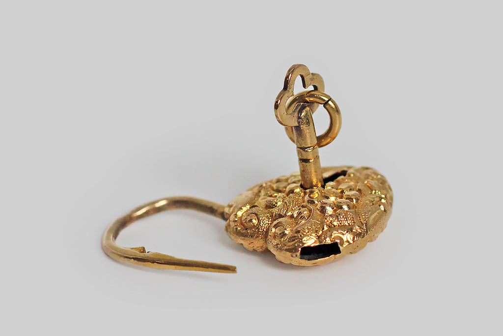 A lovely, miniature, Victorian-era, repoussé heart padlock, modeled in 14k yellow gold, and still partnered with its original 14k gold key. This functioning lock is in wonderful condition. It is highly-textural, decorated all-over with flowers and fine, swirling, baroque forms— a pair of blooms rest at the center of the pattern. This padlock would have originally been used as the focal piece for a bracelet or necklace