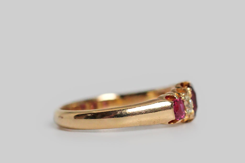 A darling, Victorian-era, five stone ring, modeled in 18k rosy yellow gold, with a tapering profile. This ring is set with three, vibrant, natural, rubies (.60 CTW) and two, cushion-shaped, old mine cut diamonds (.30 CTW)— these gemstones graduate in size, with the largest resting at the center. They are held in sculpted, split-prongs that are integral to the ring’s subtly-lobed, scalloped gallery. The ring's substaintial half-round shank tapers, somewhat, toward the base. 