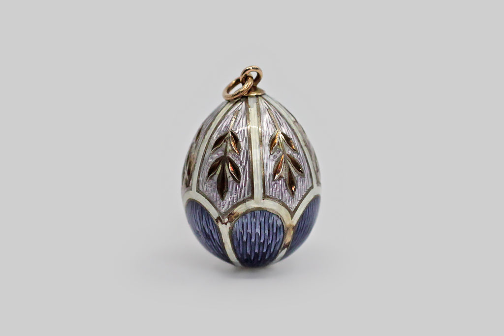 A lovely, Imperial Russian miniature egg pendant, made around the turn of the 20th century. This egg-shaped pendant is modeled in 56 zolotnik gold, and is decorated with elaborate enamel work, in lavender, periwinkle, and white. The scallop and shield-shaped guilloche enamel sections are separated by white guilloche enamel borders, and each of the lavender sections is decorated with a charming wheat motif.