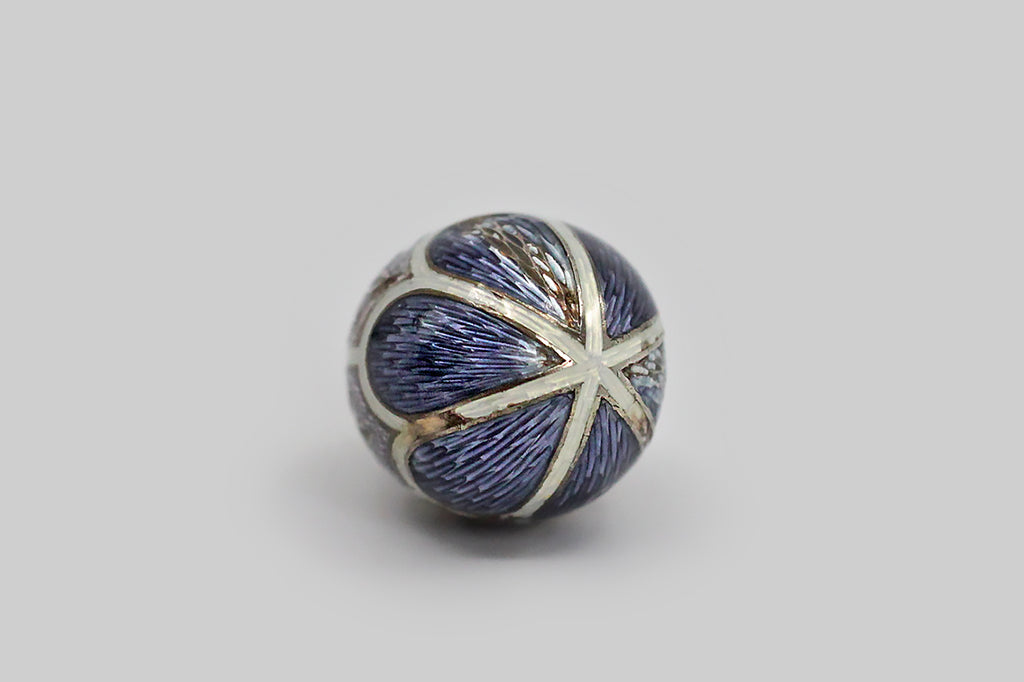 A lovely, Imperial Russian miniature egg pendant, made around the turn of the 20th century. This egg-shaped pendant is modeled in 56 zolotnik gold, and is decorated with elaborate enamel work, in lavender, periwinkle, and white. The scallop and shield-shaped guilloche enamel sections are separated by white guilloche enamel borders, and each of the lavender sections is decorated with a charming wheat motif.