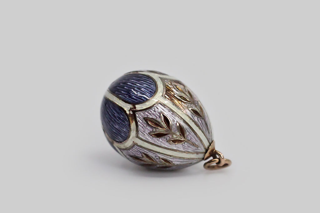 A lovely, Imperial Russian miniature egg pendant, made around the turn of the 20th century. This egg-shaped pendant is modeled in 56 zolotnik gold, and is decorated with elaborate enamel work, in lavender, periwinkle, and white. The scallop and shield-shaped guilloche enamel sections are separated by white guilloche enamel borders, and each of the lavender sections is decorated with a charming wheat motif.