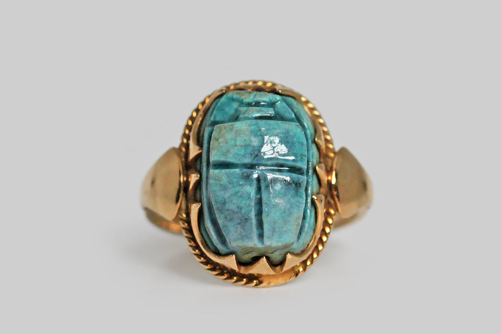 A magical, Art Deco era ring, modeled in 18k yellow gold and set with a brilliant blue, Egyptian, faience scarab bead. This talisman of renewal and rebirth is held in an ornately scalloped bezel. The foot of this festoon bezel is embellished with twisted gold wire, and the ring’s shoulders are decorated with a shapely, very minimal, lotus motif.