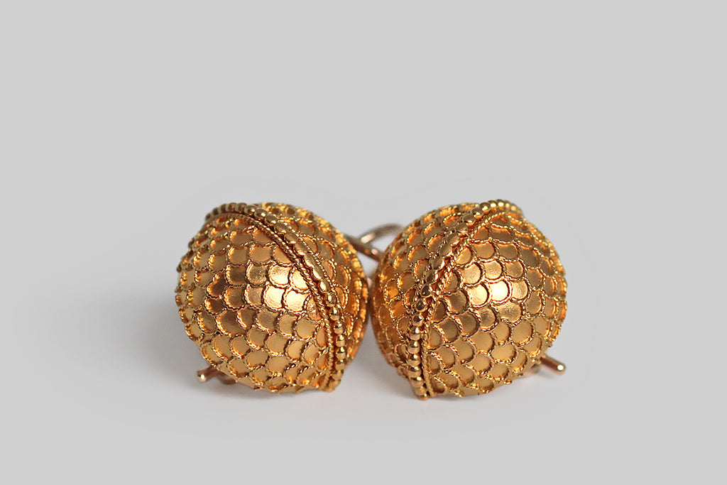A charming pair of Victorian-era drop earrings, modeled as half orbs, in 14k yellow gold. These curved faces of these orbs are covered with a delicate pattern of scallops or scales, made with applied, Etruscan-style wirework. A row of tiny granulated beads acts as an equator, dividing the orbs into hemispheres. This decor is exceptionally fine, and the perfect repetition in the design is especially winning. 