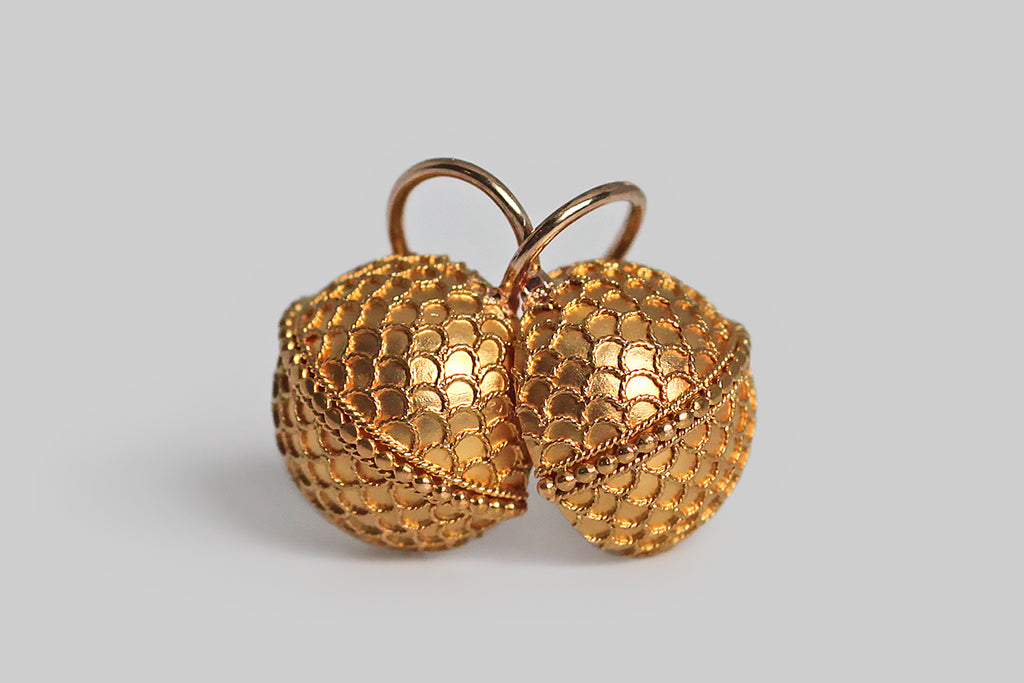 A charming pair of Victorian-era drop earrings, modeled as half orbs, in 14k yellow gold. These curved faces of these orbs are covered with a delicate pattern of scallops or scales, made with applied, Etruscan-style wirework. A row of tiny granulated beads acts as an equator, dividing the orbs into hemispheres. This decor is exceptionally fine, and the perfect repetition in the design is especially winning. 